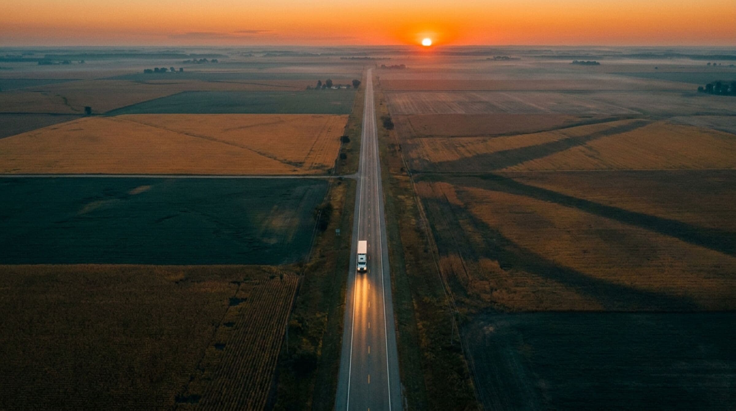 Aerial view at dusk of a lone freight truck on a rural highway cutting through farmland