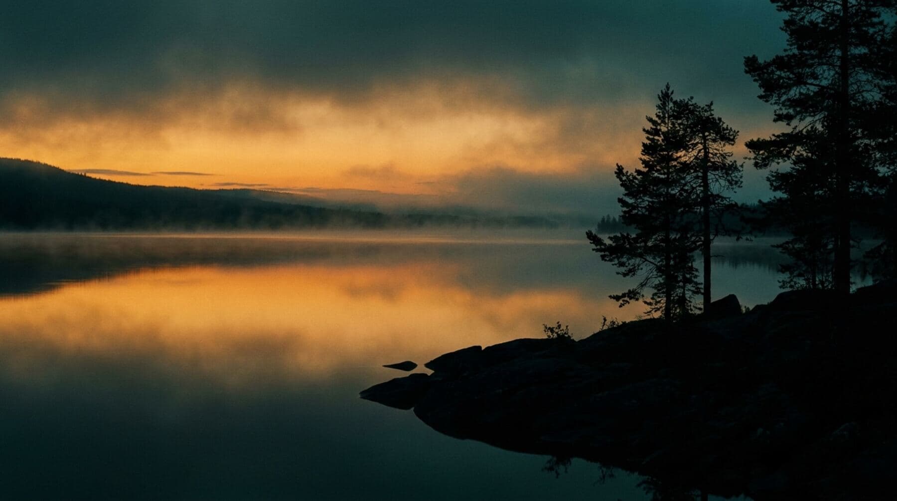 A vast still lake at dusk under an amber sky, mist over mirror-flat water